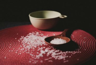 A wooden spoon with rice on a textured red mat, creating a warm, rustic feel.