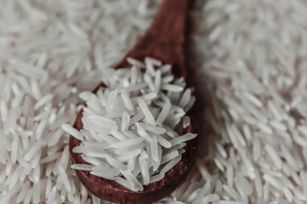 From above of raw white rice grains on wooden spoon placed on pile